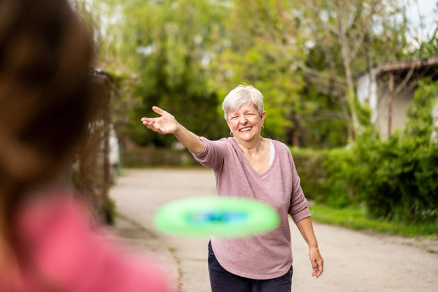 Grandmother and granddaughter playing with frisbee outside.