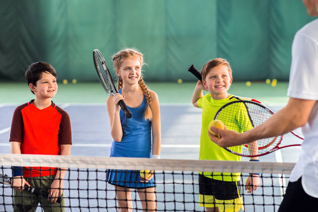 Kinderen aan net met coach op hardcore tennisveld