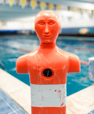 Portrait stock photo of a life saving practice dummy in front of indoors swimming pool