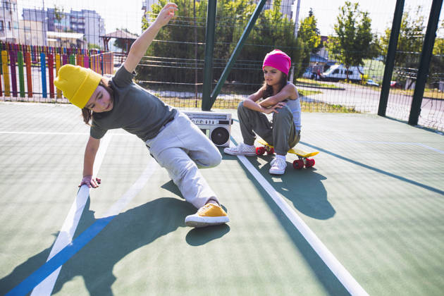Two happy children listening music, having fun and dancing breakdance on a playground.
