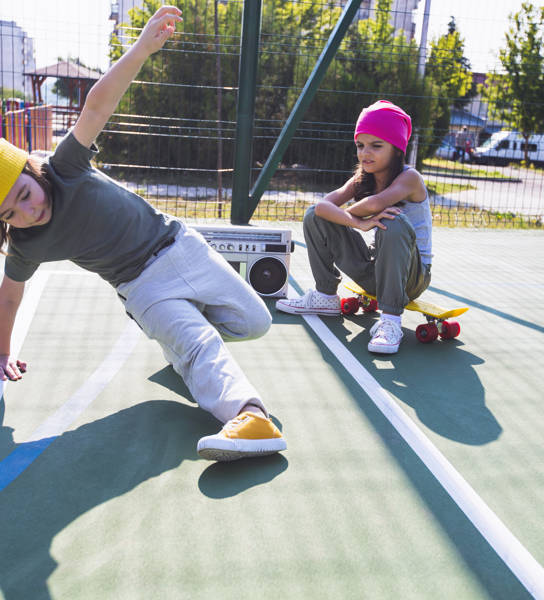 Two happy children listening music, having fun and dancing breakdance on a playground.