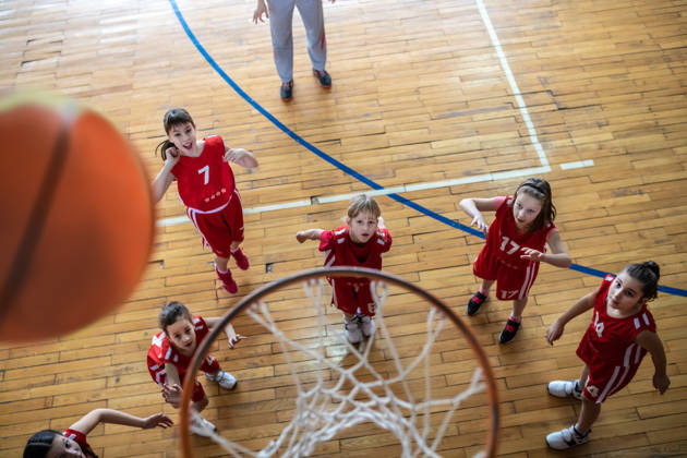 Meisjesteam gooit bal naar basketring in sporthal