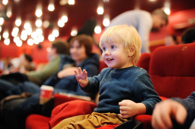 Cute toddler boy watching cartoon movie in the cinema. Leisure/entertainment for family with kids.