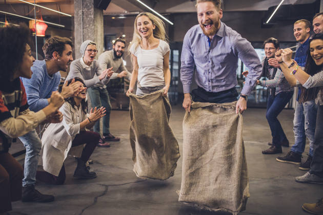 Large group of happy entrepreneurs having fun on a sack race in the office,
