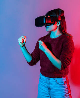 Girl wearing virtual reality glasses on head playing fighting game, holding clenched fists up ready to boxing, experiencing cyberspace using VR headset technology. colorful neon light studio shot