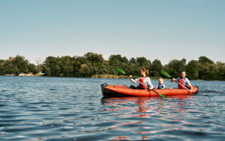 Young caucasian family floating on kayak with paddles. Concept of rest, leisure and vacation at nature. Extreme water sport. Mother, father and daughter wearing life vests. Summer sunny daytime