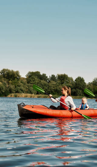 Young caucasian family floating on kayak with paddles. Concept of rest, leisure and vacation at nature. Extreme water sport. Mother, father and daughter wearing life vests. Summer sunny daytime