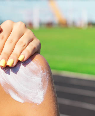 Fitness woman is applying sunscreen on her shoulder before training at the stadium. Protect your skin during sport activity.