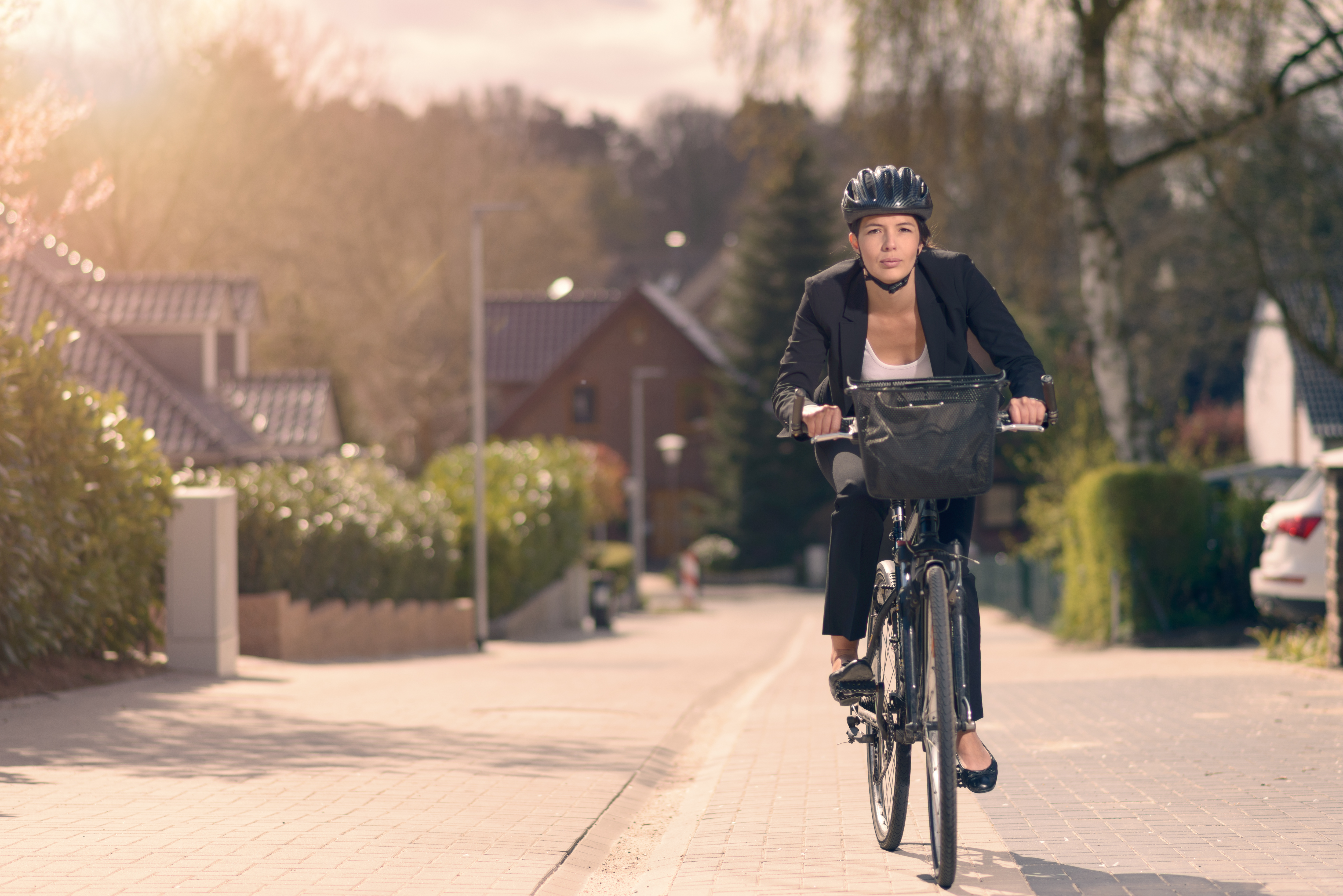 Young businesswoman riding to work on a bicycle along a residential street in her stylish slack suit and safety helmet in an eco-friendly mode of transport