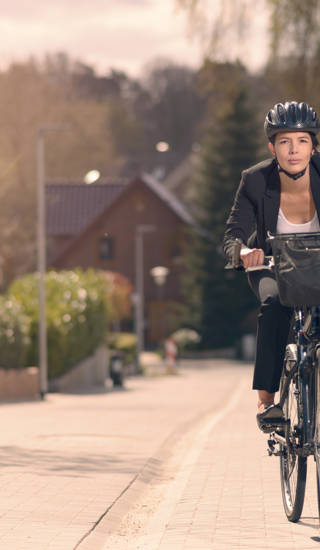 Young businesswoman riding to work on a bicycle along a residential street in her stylish slack suit and safety helmet in an eco-friendly mode of transport