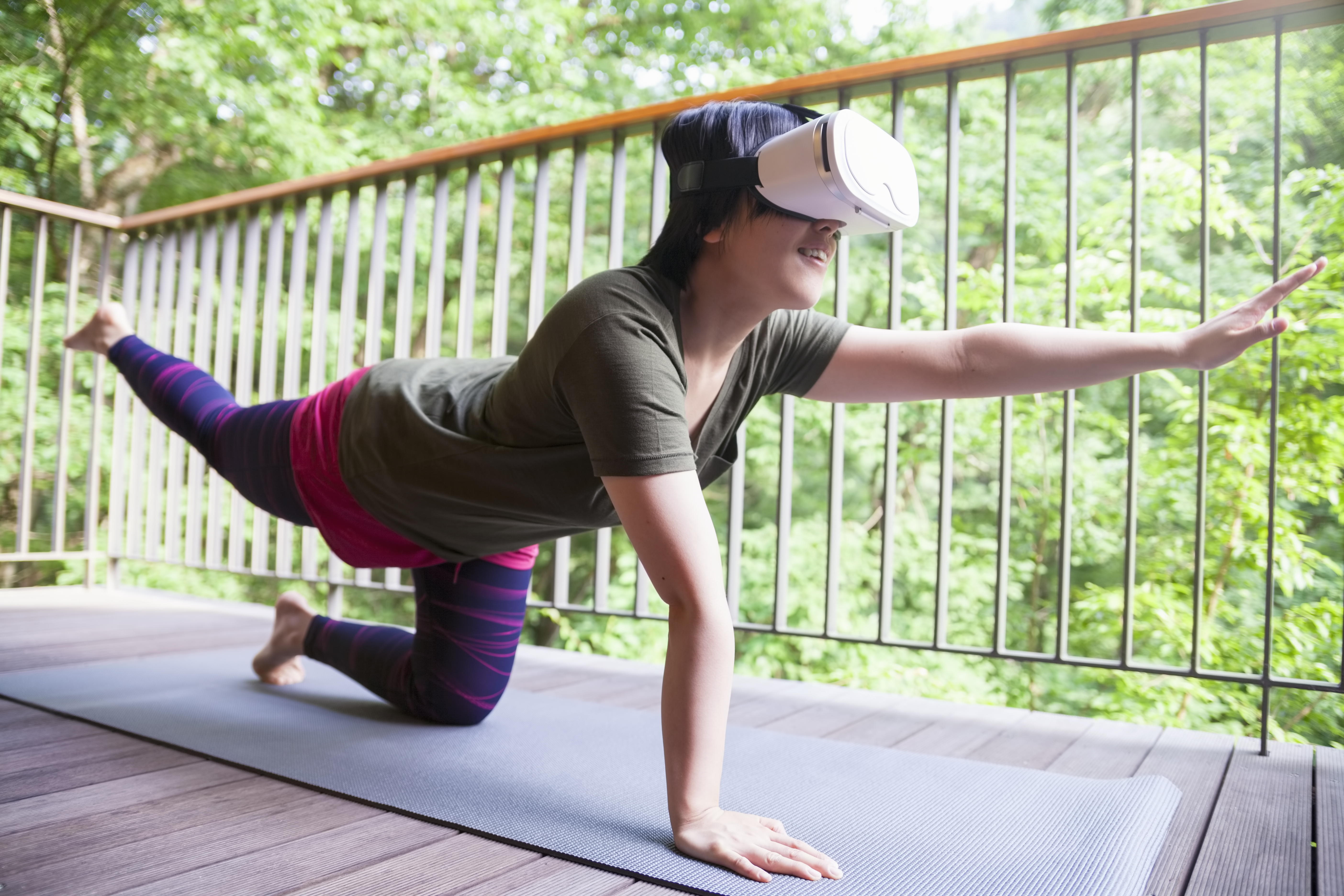 A young woman is doing yoga on balcony and wearing a virtual reality device for instructors.