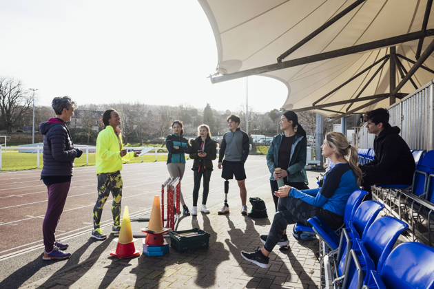 Groepje luistert naar trainer op piste, 1 man met beenprothese luistert mee