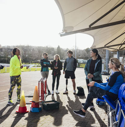 Groepje luistert naar trainer op piste, 1 man met beenprothese luistert mee