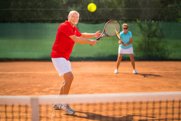 active senior couple tennis players playing double on a clay court. Logo for racket and clothing created by ourselves therefore property released