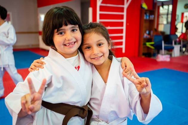 A group of elementary age children are taking a martial arts class. They are standing together in a row and are smiling while looking at the camera, Peace Sign - Gesture,