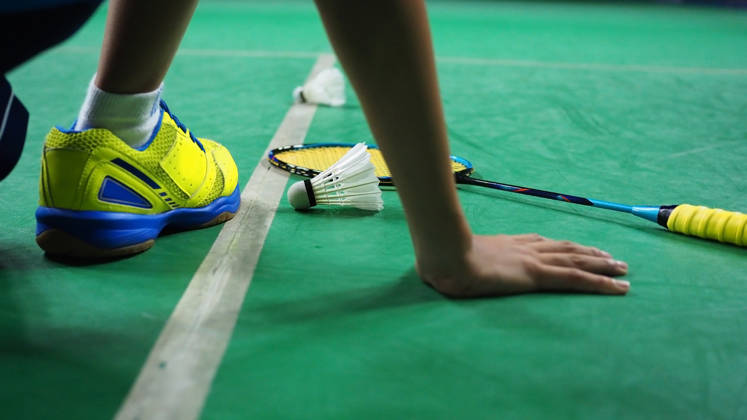 Male foot and his hand resting inside a badminton court with his racket and shuttlecock.