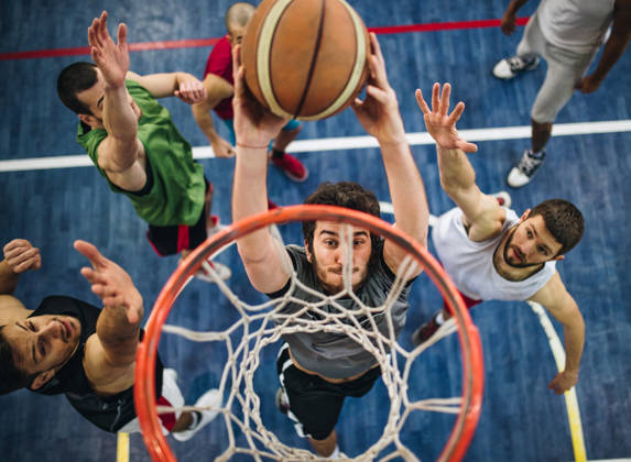 High angle view of a determined basketball player slam dunking the ball while passing through defensive players.