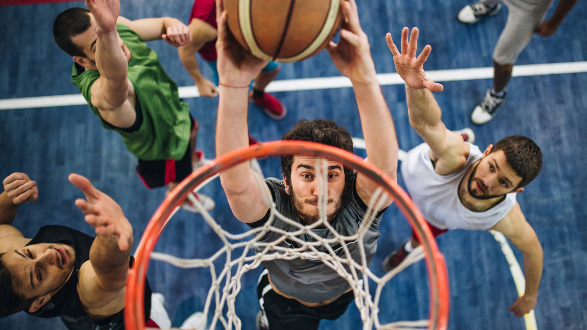 High angle view of a determined basketball player slam dunking the ball while passing through defensive players.
