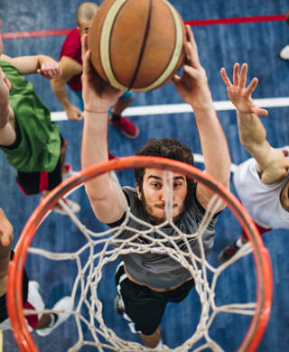 High angle view of a determined basketball player slam dunking the ball while passing through defensive players.