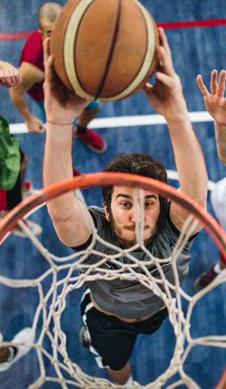 High angle view of a determined basketball player slam dunking the ball while passing through defensive players.
