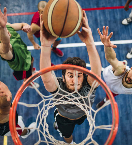 High angle view of a determined basketball player slam dunking the ball while passing through defensive players.