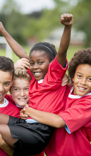 A group of children on a soccer team wearing red jerseys, celebrating their victory together.