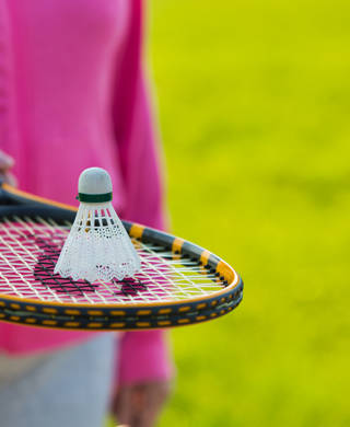Midsection of senior woman with shuttlecock on tennis bat in park