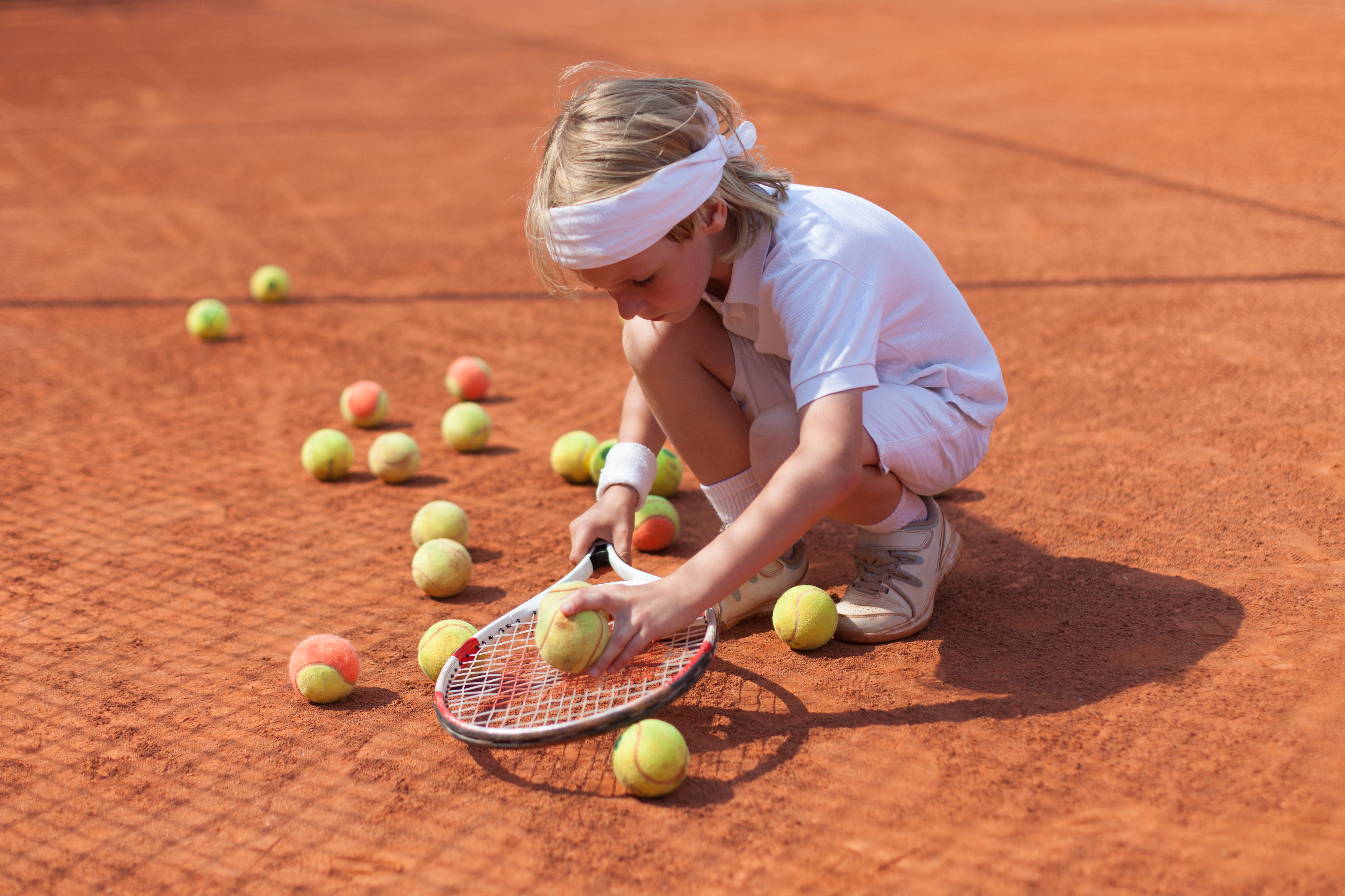 Meisje speelt met tennisballen op gravel tennisveld