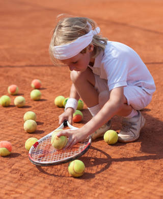 Meisje speelt met tennisballen op gravel tennisveld