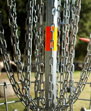 Disc golfer releases disc towards the basket for a successful putt.