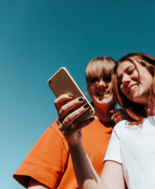Happy smiling girls together having fun. Young female student friends reading text messages together on their Mobile Phone. Laughing and Smiling while reading the posts and watching funny video clips. Young Women Outdoor Lifestyle.