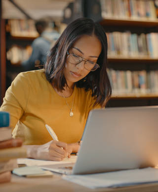 vrouw zit achter pc aan bureau met boeken opleiding leren