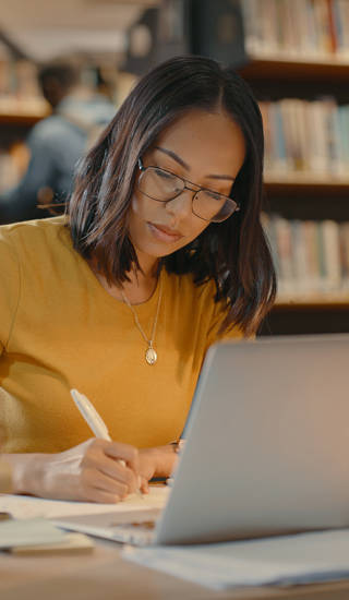 vrouw zit achter pc aan bureau met boeken opleiding leren
