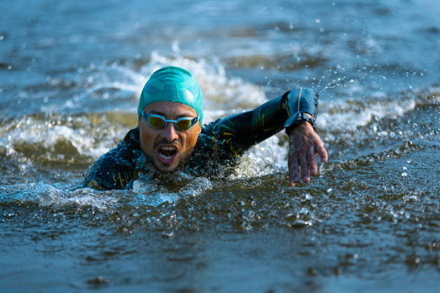 Professional triathlete swimming in river's open water. Man wearing swim equipment practicing triathlon on the beach in summer's day. Concept of healthy lifestyle, sport, action, motion and movement.