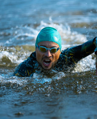 Professional triathlete swimming in river's open water. Man wearing swim equipment practicing triathlon on the beach in summer's day. Concept of healthy lifestyle, sport, action, motion and movement.