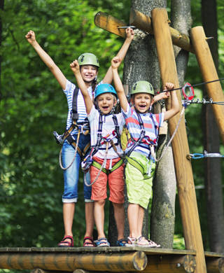 Jonge mama en twee jonge kinderen staan op platform van hoogtouwenparcours en steken armen in de lucht