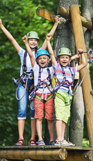 Jonge mama en twee jonge kinderen staan op platform van hoogtouwenparcours en steken armen in de lucht