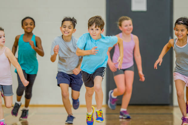 An elementary age Caucasian boy runs at the front of the group during gym class.