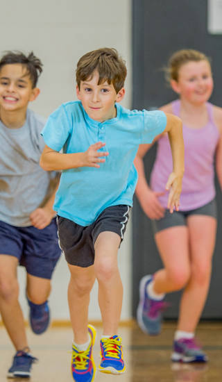 An elementary age Caucasian boy runs at the front of the group during gym class.