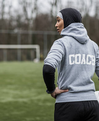 Jonge vrouwelijke voetbalcoach met hoofddoek op aan de rand van een voetbalveld