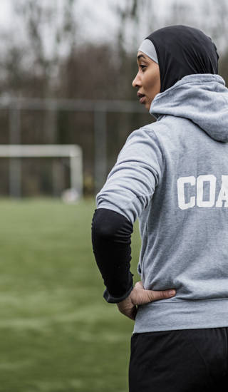 Jonge vrouwelijke voetbalcoach met hoofddoek op aan de rand van een voetbalveld
