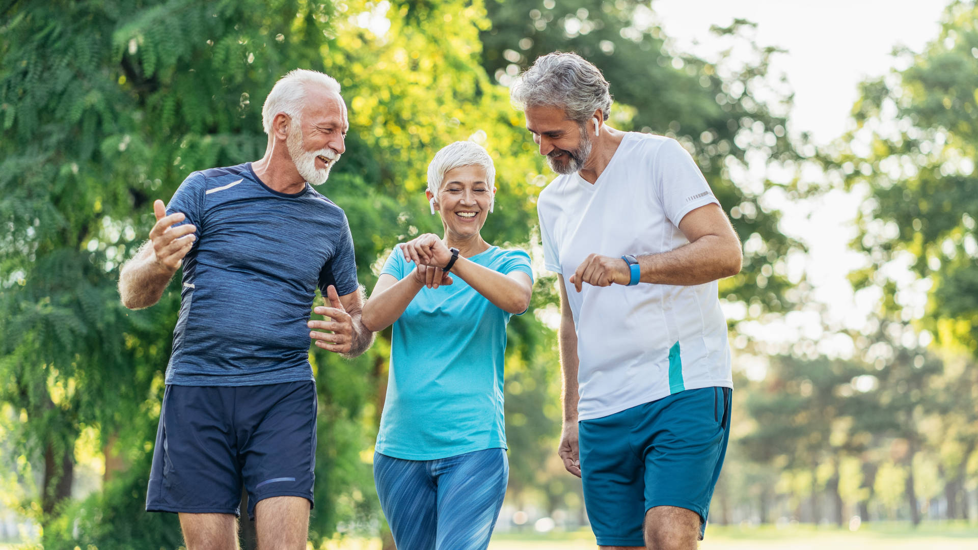 Three senior athletes in the park using digital devices after jogging