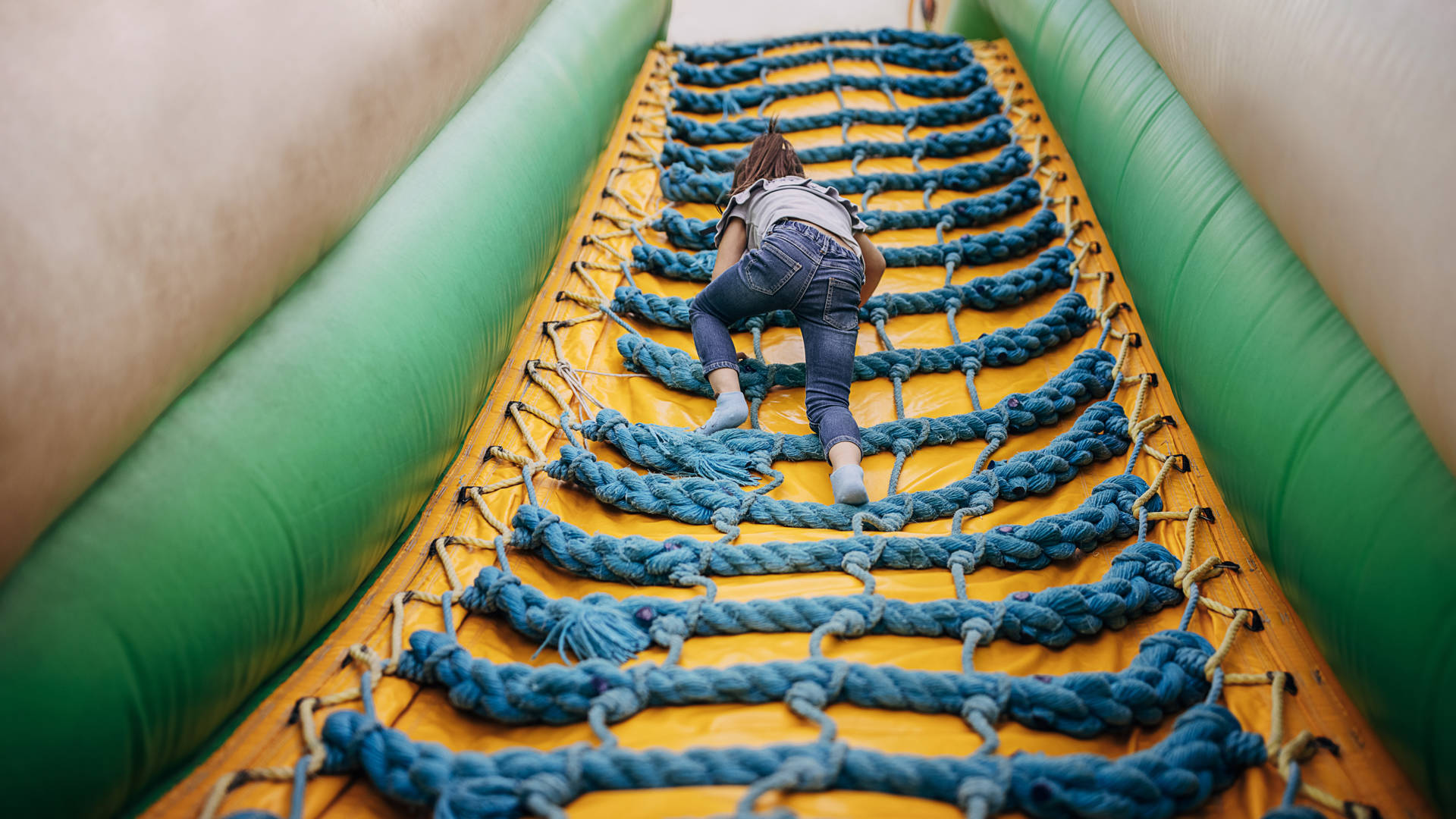 Cute little girl playing in climbing up inflatable bouncy castle in amusement park.