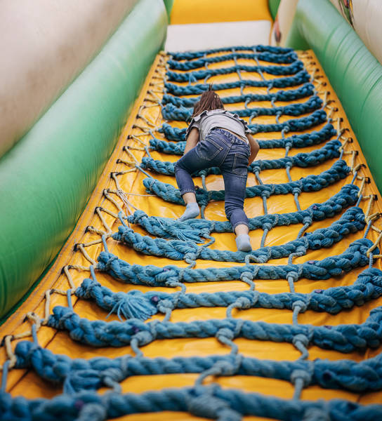 Cute little girl playing in climbing up inflatable bouncy castle in amusement park.