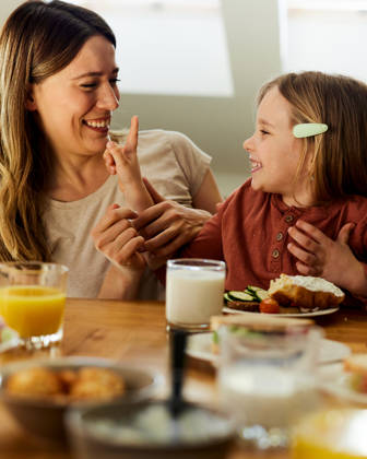 Happy mother communicating with her small girl during breakfast in dining room.