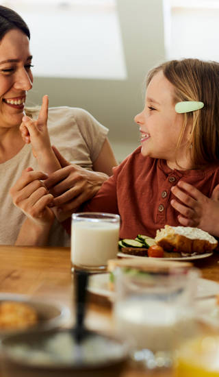 Happy mother communicating with her small girl during breakfast in dining room.
