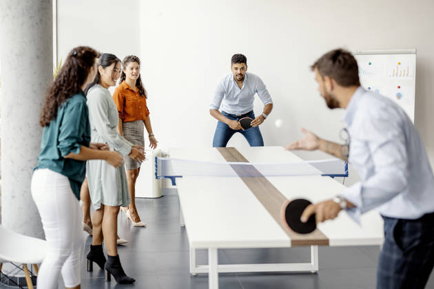Group of young startup business people playing table tennis together on a boardroom table in an office while taking a break from their meeting