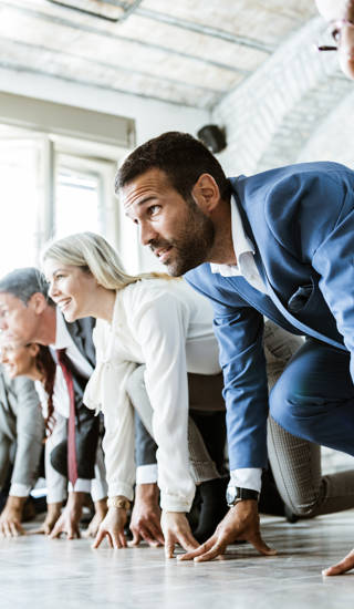 Large group of business people on a starting line ready for sports race in the office. Focus is on man in blue suit. Copy space.