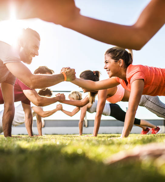 Low angle view of athletes cooperating while exercising on a sports training outdoors. Focus is happy couple.