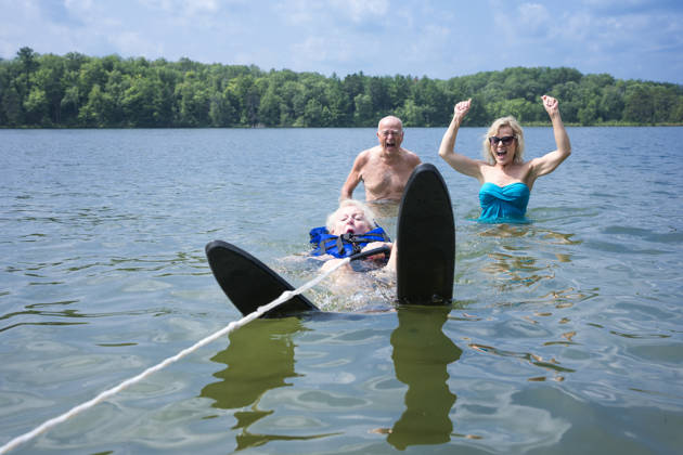 Kind op waterskilatten probeert uit water te komen en grootouders kijken toe